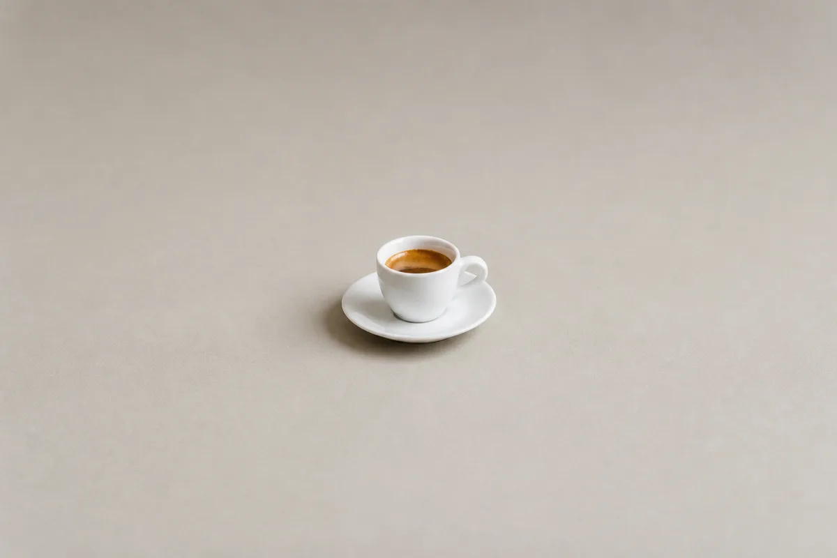 A small white espresso cup and saucer surrounded by generous empty space on a plain background