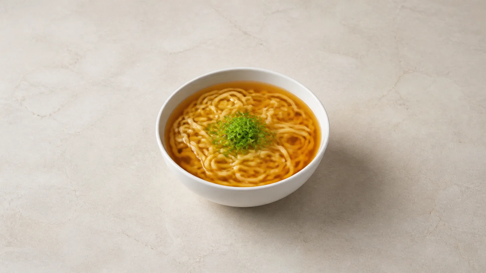 A centered bowl of ramen on a pale stone counter with soft side lighting and even open space